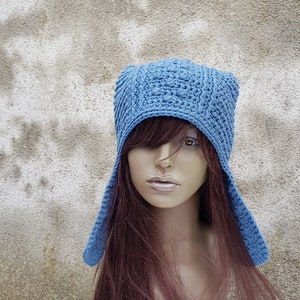 May include: A blue crocheted hat with ear flaps. The hat is made with a textured stitch and has a square shape on top.