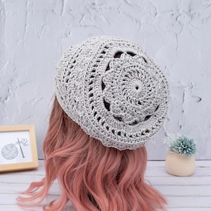 May include: A gray crocheted beanie with a large circular design on the top.