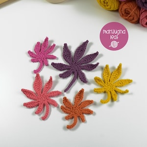 Könnte beinhalten: Sechs gehäkelte Marihuana-Blatt-Applikationen in verschiedenen Farben: Rosa, Lila, Koralle, Orange und Gelb. Die Blätter sind auf einer weißen Oberfläche angeordnet. Ein rosa Kreis mit dem Text "marijuana leaf" und einer Garnkugel-Grafik ist im Bild.
