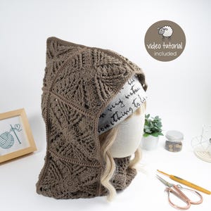 May include: A brown crocheted hooded cowl with a textured pattern. The cowl is worn on a mannequin with blonde hair. The text "video tutorial included" is visible in the top right corner of the image.