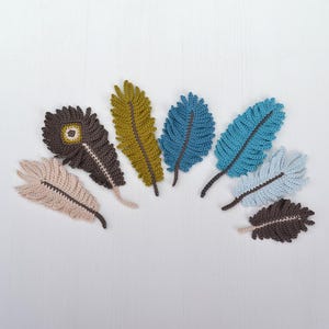 May include: A collection of seven crochet feather appliques in various colours including beige, dark brown, olive green, teal, light blue, and pale blue. Each feather features a central spine and textured, stitched edges in a fan-like shape.