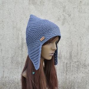 May include: A blue crocheted hat with ear flaps. The hat has a pointed crown and a small leather label with the word "Handmade" on it.
