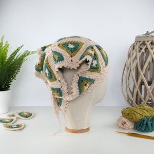 May include: A beige crochet hat with green and teal geometric patterns, displayed on a mannequin head. The hat has a scalloped edge and a tie. Several matching crochet pieces are visible, along with yarn and a crochet hook.