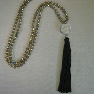 May include: A multi-strand necklace with iridescent beads and a gold chain. The necklace has a clear crystal pendant with a black tassel.