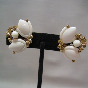 以下が含まれることがあります： 白い花の形をしたアクセントが付いた、ゴールドトーンのクリップ式イヤリングのペアです。