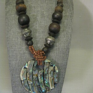 May include: A brown wood bead necklace with a large iridescent abalone shell pendant and matching earrings. The necklace has silver accents and a brown and orange braided cord.