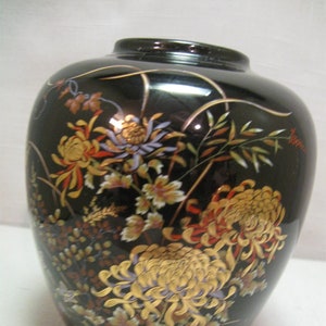 May include: Black ceramic vase with gold and red floral designs. The vase features a variety of flowers, including chrysanthemums, and leaves.