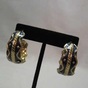 Könnte beinhalten: Ein Paar goldene Creolen mit blauen, grünen und roten Emaille-Details. Die Ohrringe befinden sich auf einem schwarzen Präsentationsständer.