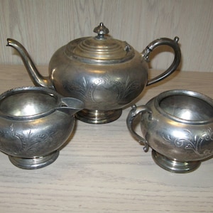 Puede incluir: Un juego de té de plata con tetera, jarra de crema y azucarero. Cada pieza presenta un diseño floral adornado.