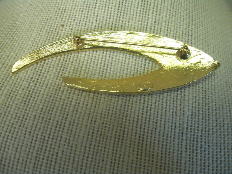May include: Gold-toned metal brooch shaped like a crescent moon with a textured surface. The back of the brooch has a small, round, metal stamp with the text "Made in Italy".