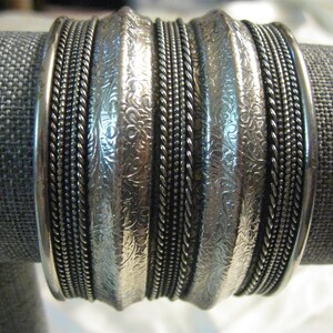 May include: A silver bracelet with multiple bands, each with a different textured design. The bands are stacked on top of each other and have a shiny finish.