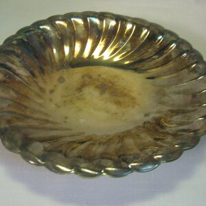 May include: A tarnished, oval-shaped silver dish with a scalloped edge. The dish has a ridged design radiating from the center. The interior shows signs of wear and discoloration, adding to its vintage appeal. A decorative piece.