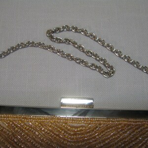 Puede incluir: Un peque&ntilde;o bolso de noche de cuentas con una correa de cadena plateada. El bolso est&aacute; hecho de una tela marr&oacute;n claro y tiene un cierre plateado.