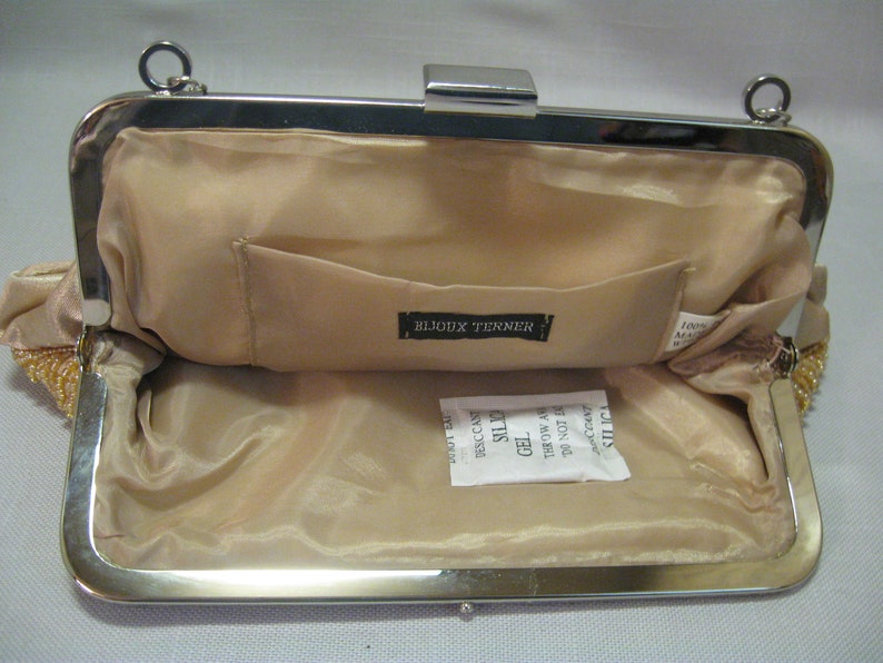 Puede incluir: Un bolso de mano de noche de cuentas beige con un marco y cierre plateados. El interior est&aacute; forrado con una tela beige y tiene un bolsillo peque&ntilde;o. El bolso tiene una etiqueta que dice "Bijoux Terner".