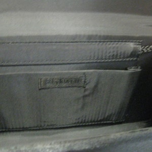 May include: Black fabric clutch purse with a zipper closure and a small pocket on the inside. The purse has a black fabric lining and a black fabric strap.