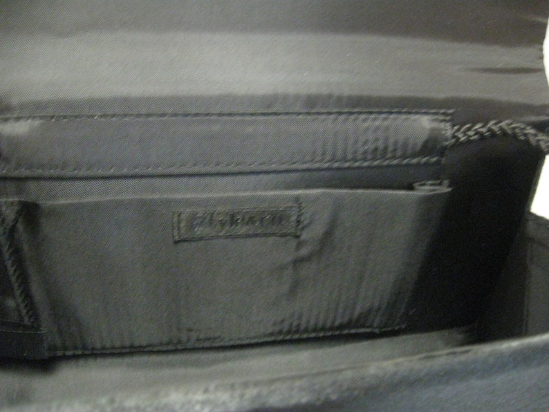 May include: Black fabric clutch purse with a zipper closure and a small pocket on the inside. The purse has a black fabric lining and a black fabric strap.