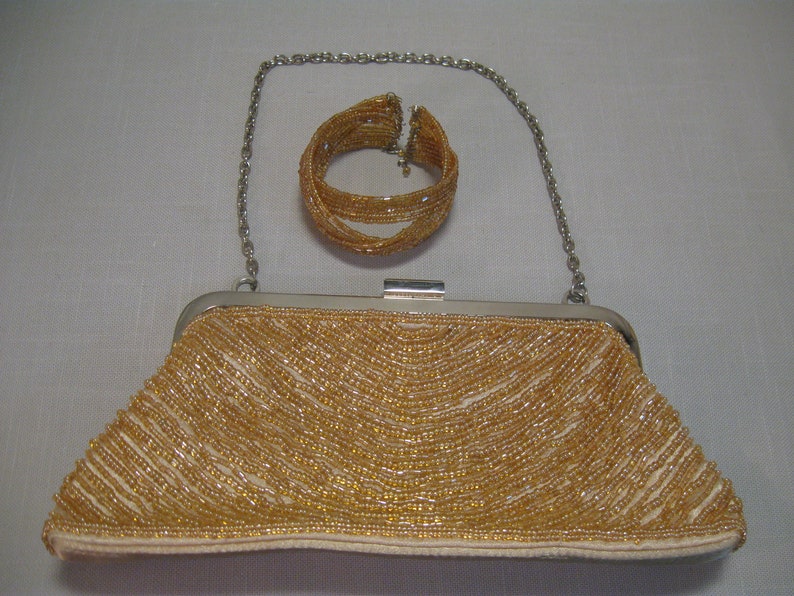 Puede incluir: Un bolso de mano de cuentas doradas con un brazalete de cuentas doradas a juego y una correa de cadena plateada.