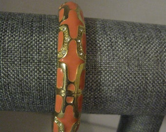 May include: A coral and gold bangle bracelet with a geometric pattern and clear rhinestones.