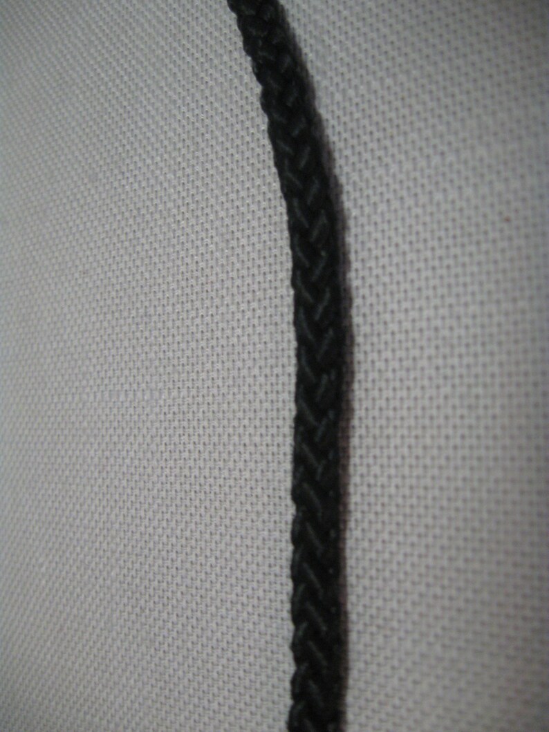 May include: A close-up of a black braided cord against a white textured background.