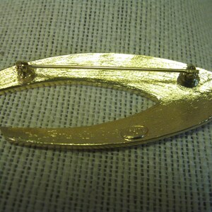 May include: Gold-toned metal brooch in the shape of a crescent moon. The back of the brooch has a pin and a clasp. The brooch is marked "Made in Italy".