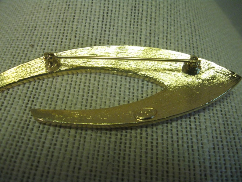 May include: Gold-toned metal brooch in the shape of a crescent moon. The back of the brooch has a pin and a clasp. The brooch is marked "Made in Italy".