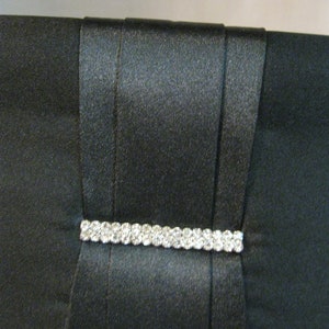 May include: A black satin clutch with a rhinestone embellishment.