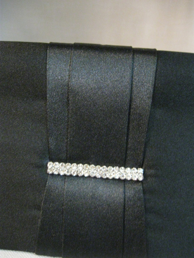 May include: A black satin clutch with a rhinestone embellishment.