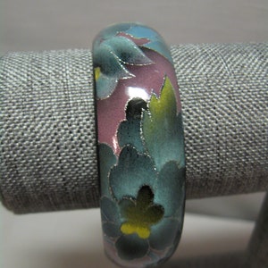 May include: A blue, pink and green floral bangle bracelet. The bracelet is made of a smooth, shiny material and features a floral design with a yellow centre.