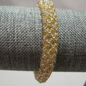May include: A gold beaded bracelet with iridescent beads. The bracelet is on a gray fabric background.