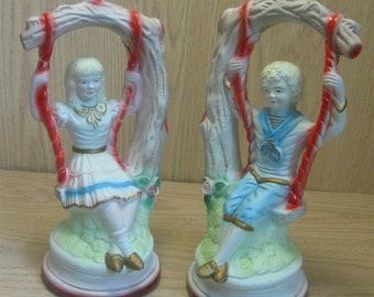 Figurine Set Peint à la main Paire de céramique Garçon portant un costume de marin Knickers bleus et une fille portant une robe chacun sur une balançoire des années 1950