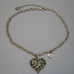 May include: A gold chain necklace with a large black and gold heart pendant featuring a leopard print design. The pendant is embellished with small clear rhinestones. The necklace also includes a smaller gold heart charm with clear rhinestones.