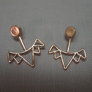 Puede incluir: Un par de pendientes de aro dorados con un diseño geométrico. Los aros son de metal fino y tienen un aspecto delicado y moderno.