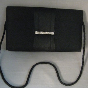 May include: A black satin clutch with a rhinestone clasp and a black braided strap.