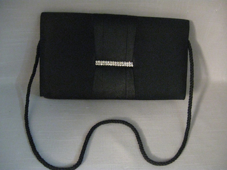 May include: A black satin clutch with a rhinestone clasp and a black braided strap.