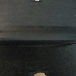 May include: A black fabric clutch purse with two silver metal snap closures.