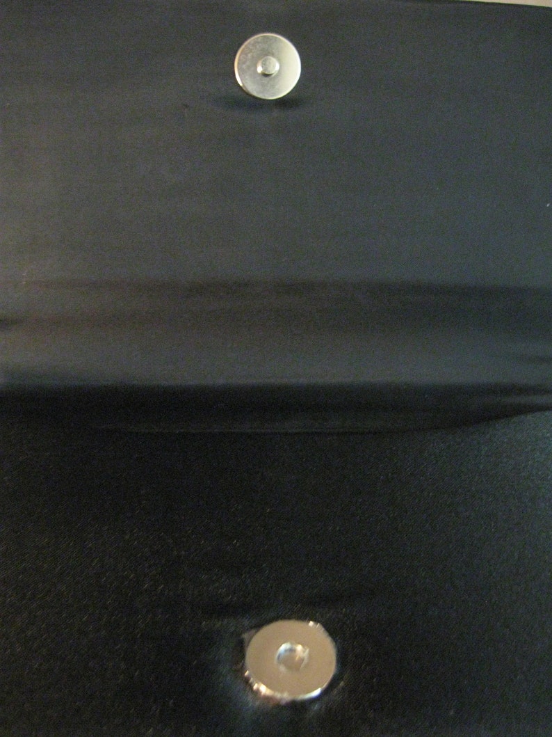 May include: A black fabric clutch purse with two silver metal snap closures.