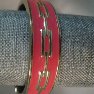 May include: A pink bangle bracelet with a gold chain design. The bracelet is made of metal and has a shiny finish.