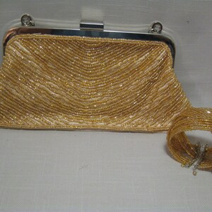 Puede incluir: Un bolso de mano de cuentas doradas con una pulsera de cuentas a juego. El bolso tiene un marco y un cierre plateados.