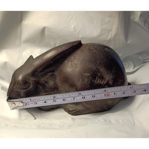 May include: A dark brown, solid-colored rabbit figurine in a resting position. A measuring tape is placed across the front, indicating a length of approximately 5 inches. The rabbit has long, laid-back ears and a smooth, matte-textured surface finish.