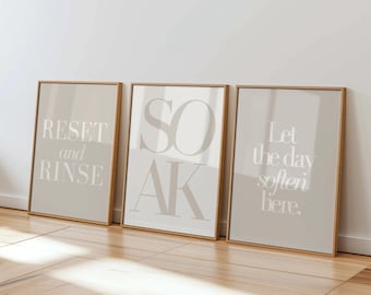 May include: Three framed art prints with text: "RESET and RINSE", "SOAK", and "Let the day soften here." The prints have a neutral color palette with beige backgrounds and light text, set in wooden frames.