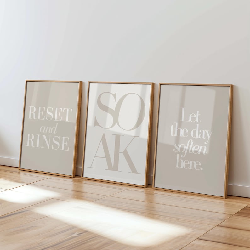 May include: Three framed art prints with text: "RESET and RINSE", "SOAK", and "Let the day soften here." The prints have a neutral color palette with beige backgrounds and light text, set in wooden frames.