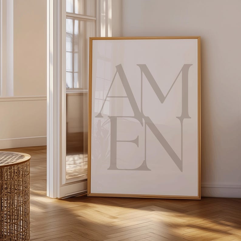 Może przedstawiać: Oprawiony wydruk z napisem "AMEN" w dużych, stylizowanych, szarych literach. Grafika umieszczona jest na jasnym tle i oprawiona w naturalnym odcieniu drewna. Wydruk eksponowany jest w jasnym pomieszczeniu z drewnianą podłogą.
