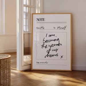 以下が含まれることがあります： 上部に「NOTE」という文字が入った額入りのプリント。テキストは「From: Me To: Myself」と「I am becoming the women of my dreams」と書かれています。日付「everyday」が下にあります。フレームは薄茶色です。