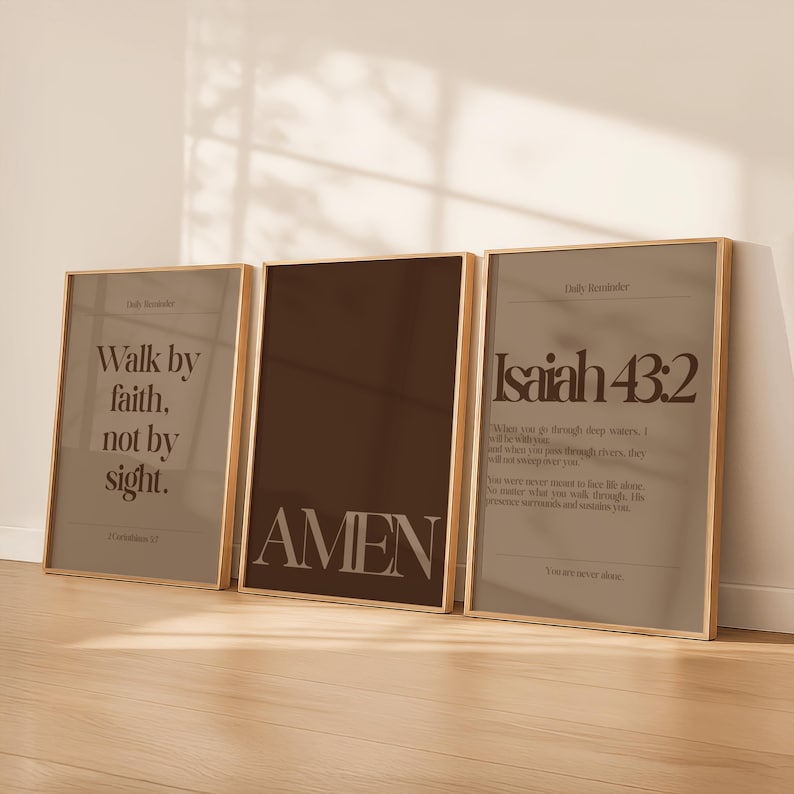 May include: Three framed prints with gold-colored frames. The left print reads "Walk by faith, not by sight." The center print says "AMEN." The right print features the text "Isaiah 43:2" and a Bible verse. The prints have a neutral color palette.