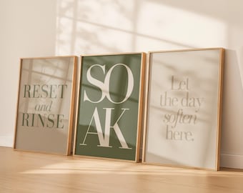 May include: Three rectangular wall art prints in light wood frames. The left print is beige with dark green text reading RESET and RINSE. The center print is dark green with white text reading SOAK. The right print is cream with beige text reading Let the day soften here.