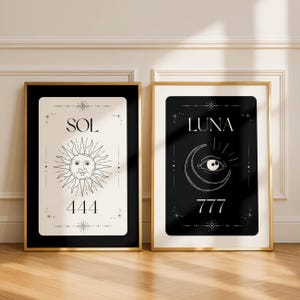 May include: Two framed art prints. One features a sun design with the word "SOL" and the number "444". The other print has a crescent moon with an eye design, the word "LUNA", and the number "777". Both are in gold frames.