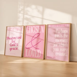 May include: Three framed art prints with gold frames. The prints feature pink backgrounds with white and pink text. The first print reads "Guest Check Protected by God's grace." The second print says "Chosen & Loved." The third print reads "The Good News Daily Perhaps this is the moment for which you were created."