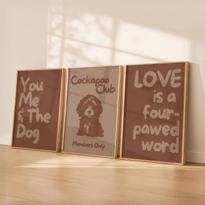 Könnte beinhalten: Drei gerahmte Kunstdrucke mit braunen Hintergründen und goldenen Rahmen. Die Drucke zeigen Text und eine Hundeillustration. Einer lautet "You Me & The Dog", ein anderer "Cockapoo Club Members Only" und der dritte "LOVE is a four-pawed word".