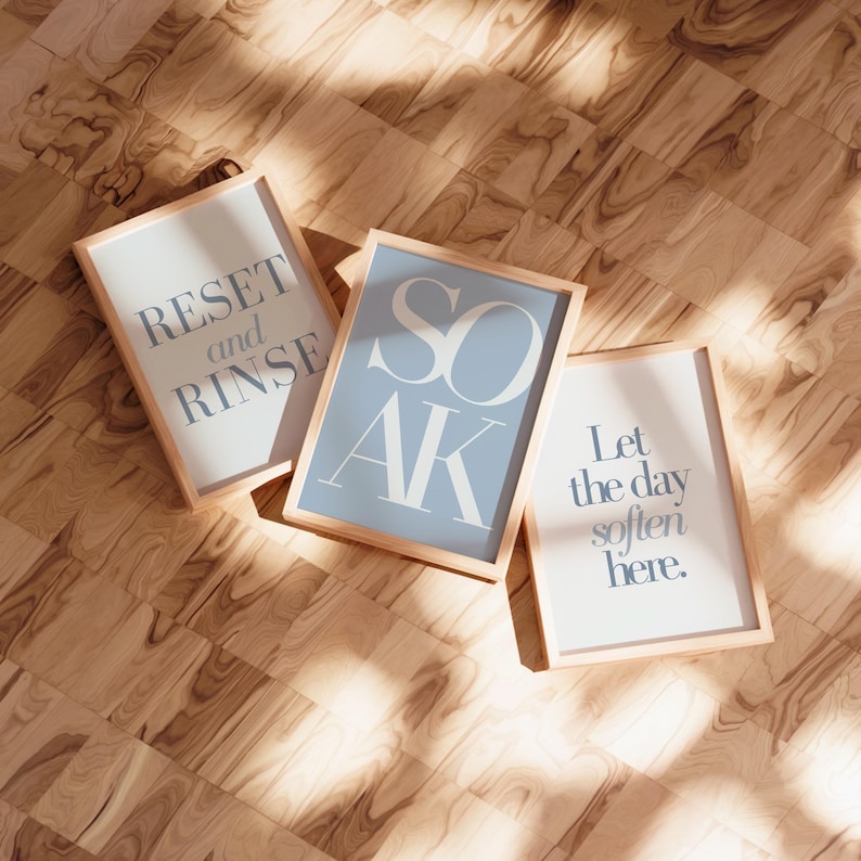 May include: Three framed prints with light wood frames. The prints have a light blue and white color scheme. The text on the prints reads: "RESET and RINSE", "SOAK", and "Let the day soften here."