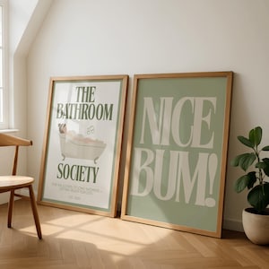 May include: Two framed art prints. One features a bathtub illustration with the text "THE BATHROOM SOCIETY" and "FOR THE LOVERS OF LONG SHOWERS + GETTING READY PLAYLISTS". The other print says "NICE BUM!" in large white letters on a sage green background.